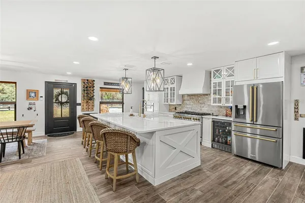 a kitchen with stainless steel appliances kitchen island granite countertop a refrigerator a stove a dining table and chairs with wooden floor