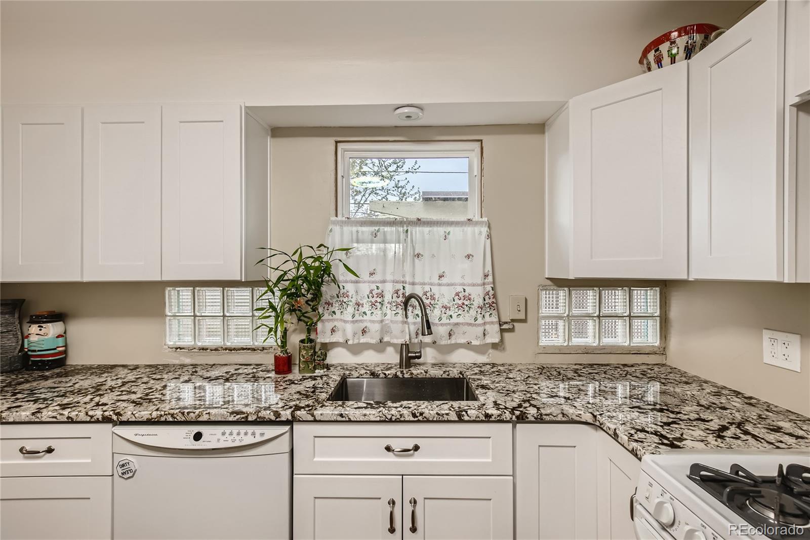 a kitchen with granite countertop a stove a sink and white cabinets