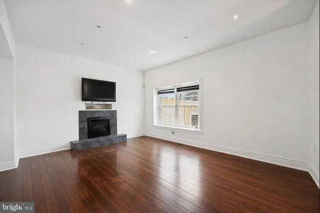 a view of an empty room with wooden floor and a fireplace