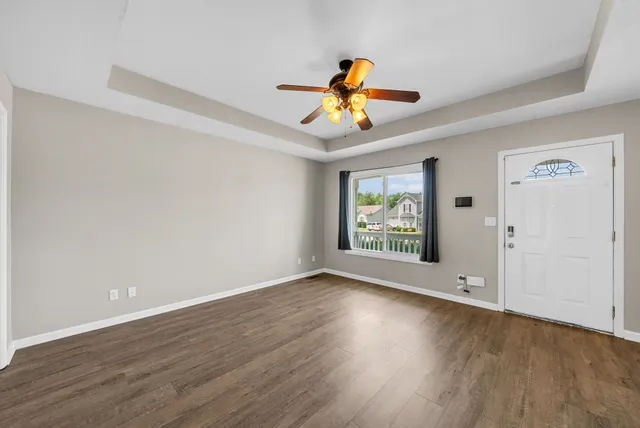 a view of an empty room with wooden floor and fan
