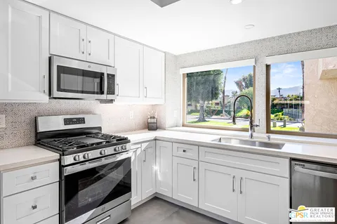 a kitchen with granite countertop white cabinets appliances and a window