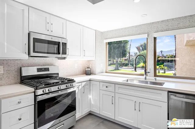 a kitchen with granite countertop white cabinets appliances and a window
