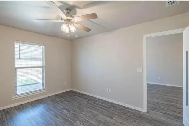 an empty room with wooden floor fan and windows