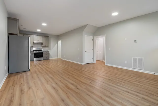 a view of empty room with wooden floor and kitchen