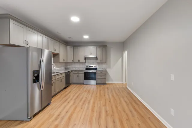 a kitchen with granite countertop a refrigerator oven a sink dishwasher and white cabinets with wooden floor