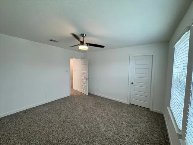 an empty room with chandelier fan and windows