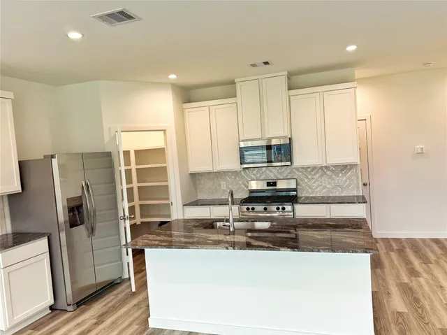 a kitchen with stainless steel appliances granite countertop a refrigerator a stove a sink and white cabinets with wooden floor