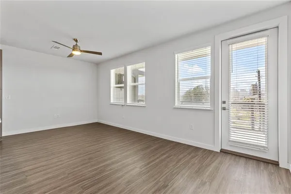 an empty room with wooden floor ceiling fan and windows