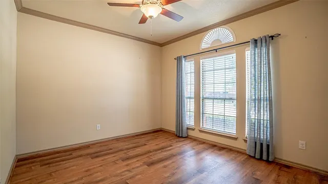 an empty room with wooden floor chandelier fan and windows
