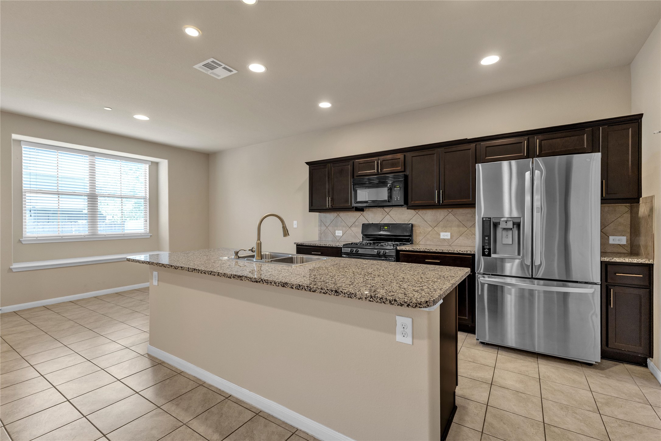 2880 Donnell Drive, Unit 2003 Round Rock, TX 78664 - Photo 9 of 31 Kitchen featuring a large island with a gooseneck faucet and granite countertop, stainless steel appliances, dark wood cabinetry, recessed lighting, and tile flooring