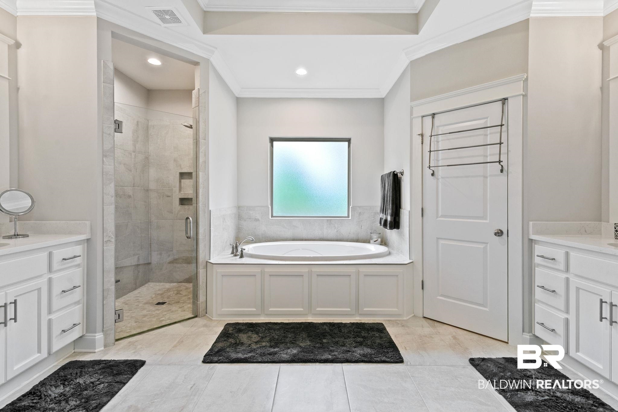 13233 Ibis Boulevard Daphne, AL 36527 - Photo 29 of 100 Spacious bathroom featuring a built-in soaking tub, a frameless glass shower enclosure with tiled walls, and two separate vanity areas with white cabinetry and light-colored countertops
