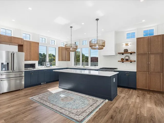 a kitchen with stainless steel appliances kitchen island granite countertop a refrigerator a stove and a wooden floors