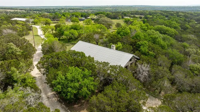 an aerial view of residential house with outdoor space and trees all around