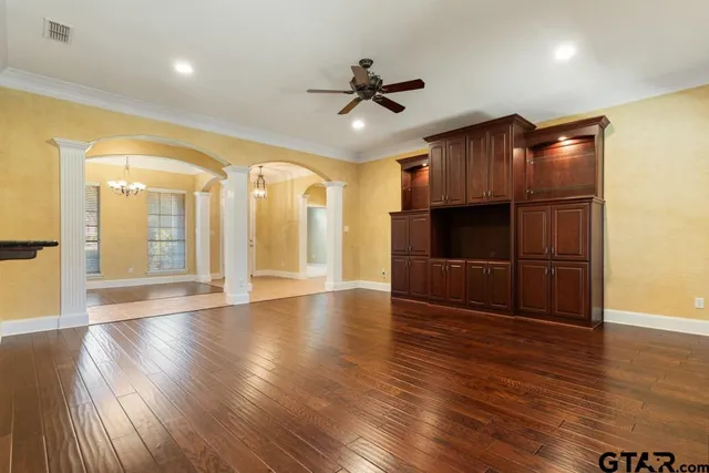a view of an empty room with wooden floor and a kitchen