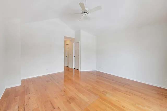 an empty room with wooden floor ceiling fan and windows