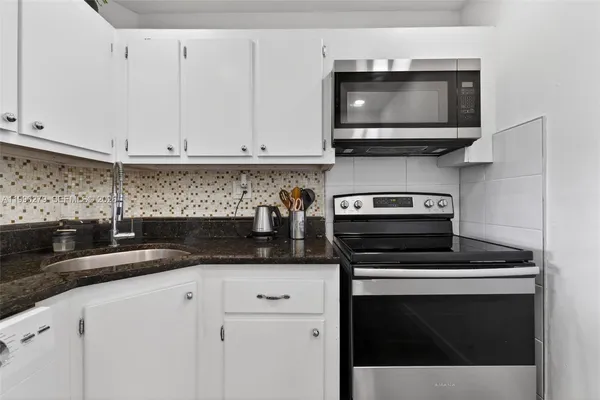 a kitchen with granite countertop white cabinets and a stove top oven