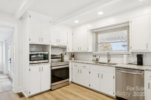 a kitchen with granite countertop stainless steel appliances white cabinets granite counter tops and a wooden floors