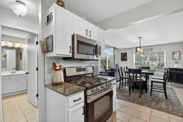 a kitchen with stainless steel appliances granite countertop a stove top oven a sink a dining table and chairs with wooden floor