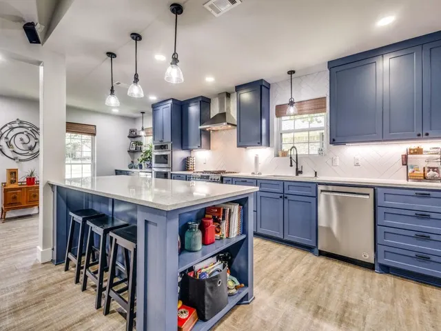 a kitchen with stainless steel appliances granite countertop wooden floors wooden cabinets a center island and chairs