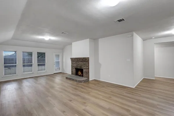 a view of an empty room with wooden floor and a fireplace