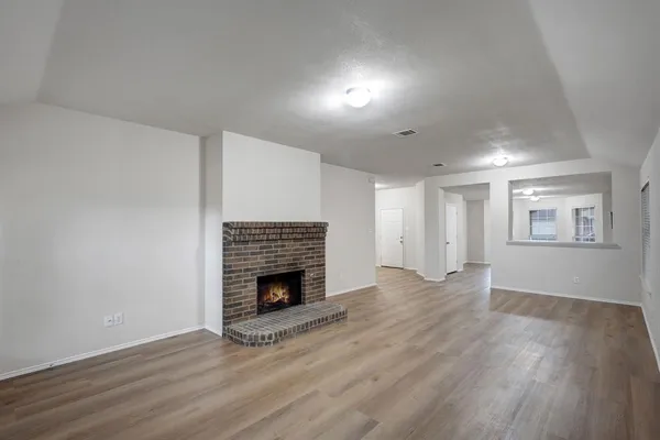 a view of an empty room with wooden floor fireplace and a window