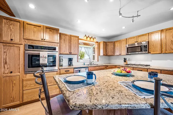 a kitchen with stainless steel appliances granite countertop a stove top oven a sink a dining table and chairs with wooden floor