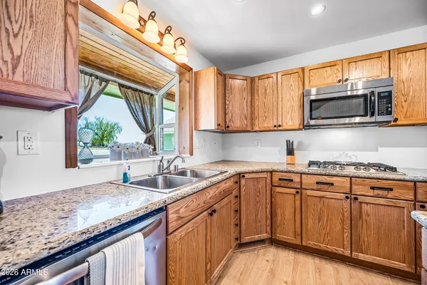 a kitchen with granite countertop a sink stainless steel appliances wooden floor and a window