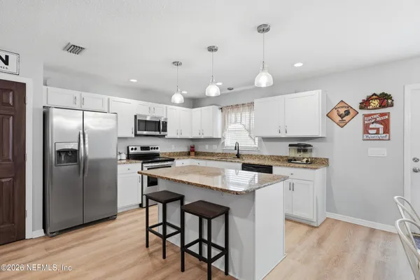 a kitchen with stainless steel appliances granite countertop a refrigerator a sink dishwasher a stove and white cabinets with wooden floor