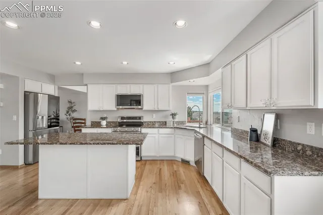 a kitchen with stainless steel appliances granite countertop a stove top oven a sink dishwasher a refrigerator and white cabinets with wooden floor