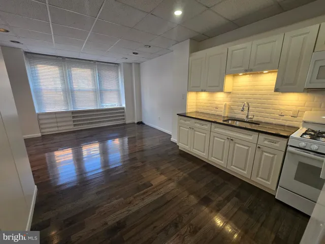 a kitchen with granite countertop a stove a sink and white cabinets