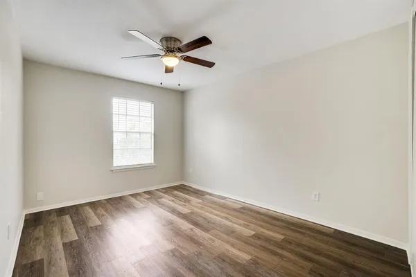 an empty room with wooden floor fan and windows