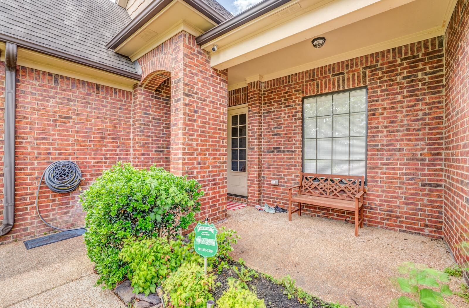 4671 Hampton Ridge Lane Bartlett, TN 38002 - Photo 6 of 40 Brick exterior featuring a covered porch, an arched doorway, a large gridded window, and mature landscaping