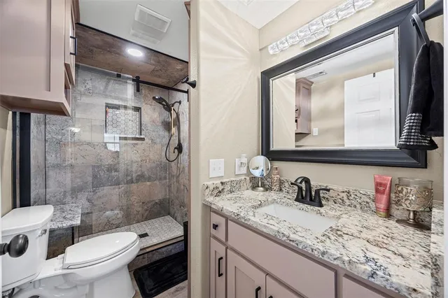 a bathroom with a granite countertop sink a toilet a mirror and shower