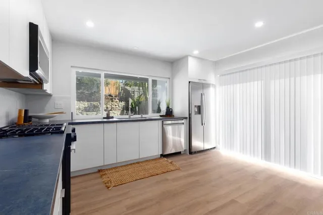 a kitchen with stainless steel appliances granite countertop a refrigerator a stove a sink and a large window