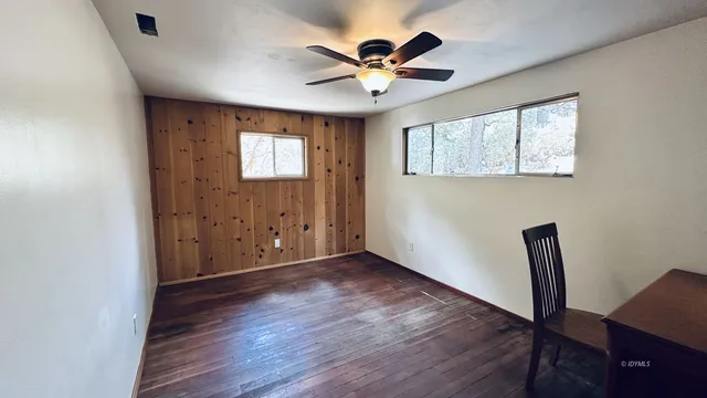 an empty room with wooden floor chandelier fan and windows
