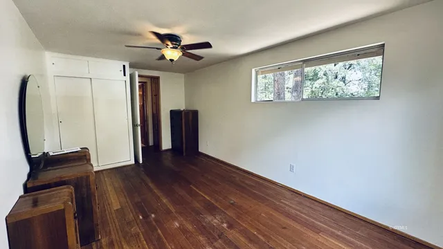a view of an empty room with wooden floor and a ceiling fan