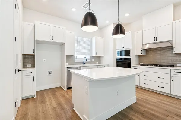 a kitchen with stainless steel appliances a stove a sink and white cabinets with wooden floor