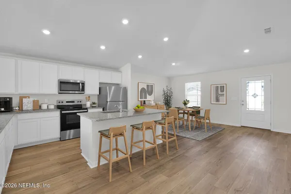 a kitchen with a dining table chairs wooden floor appliances and cabinets