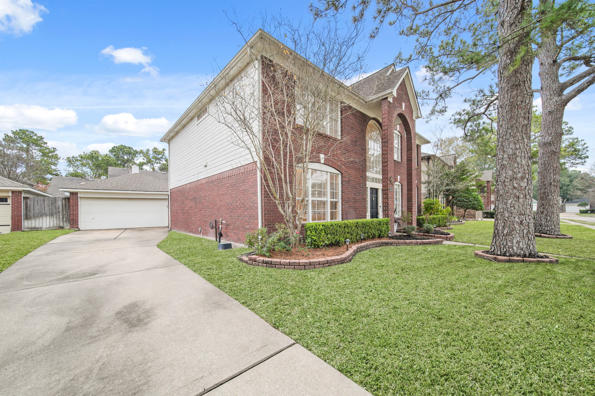 16114 Kintyre Point Road Houston, TX 77095 - Photo 3 of 44 This photo showcases a two-story brick house with large arched windows and a well-maintained front yard. The driveway leads to a detached garage, and the property is lined with mature trees, offering a welcoming and elegant curb appeal.