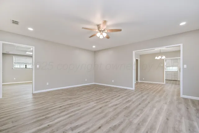 a view of an empty room with wooden floor and a ceiling fan