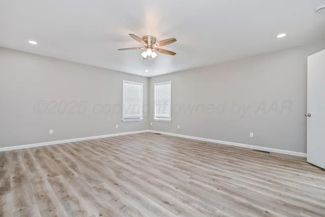 a view of an empty room with wooden floor and a ceiling fan