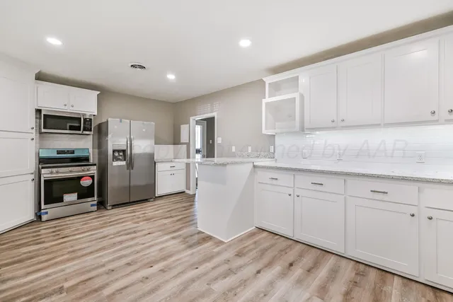 a kitchen with granite countertop a refrigerator oven a sink dishwasher and white cabinets with wooden floor