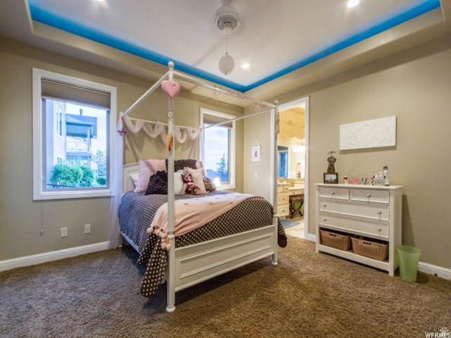 4378 Foothill Drive Bountiful, UT 84010 - Photo 22 of 46 Recessed lighting and a tray ceiling with accent lighting illuminate this carpeted room, featuring white baseboards, two windows with blinds, and a doorway opening to a bathroom with a vanity