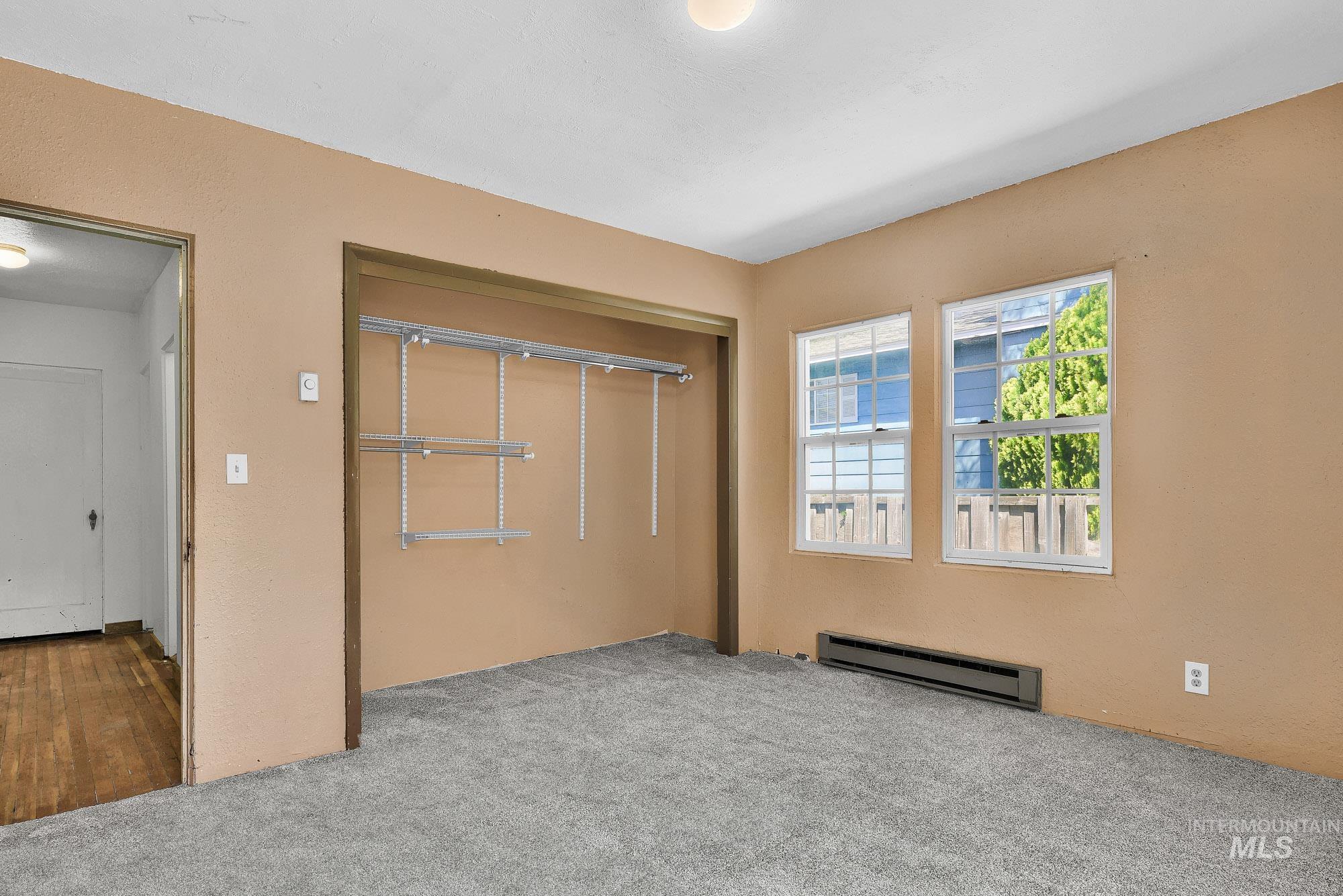 808 North A Street Parma, ID 83660 - Photo 12 of 29 Carpeted room featuring two double-hung windows, a baseboard heater, and an open closet with adjustable shelving