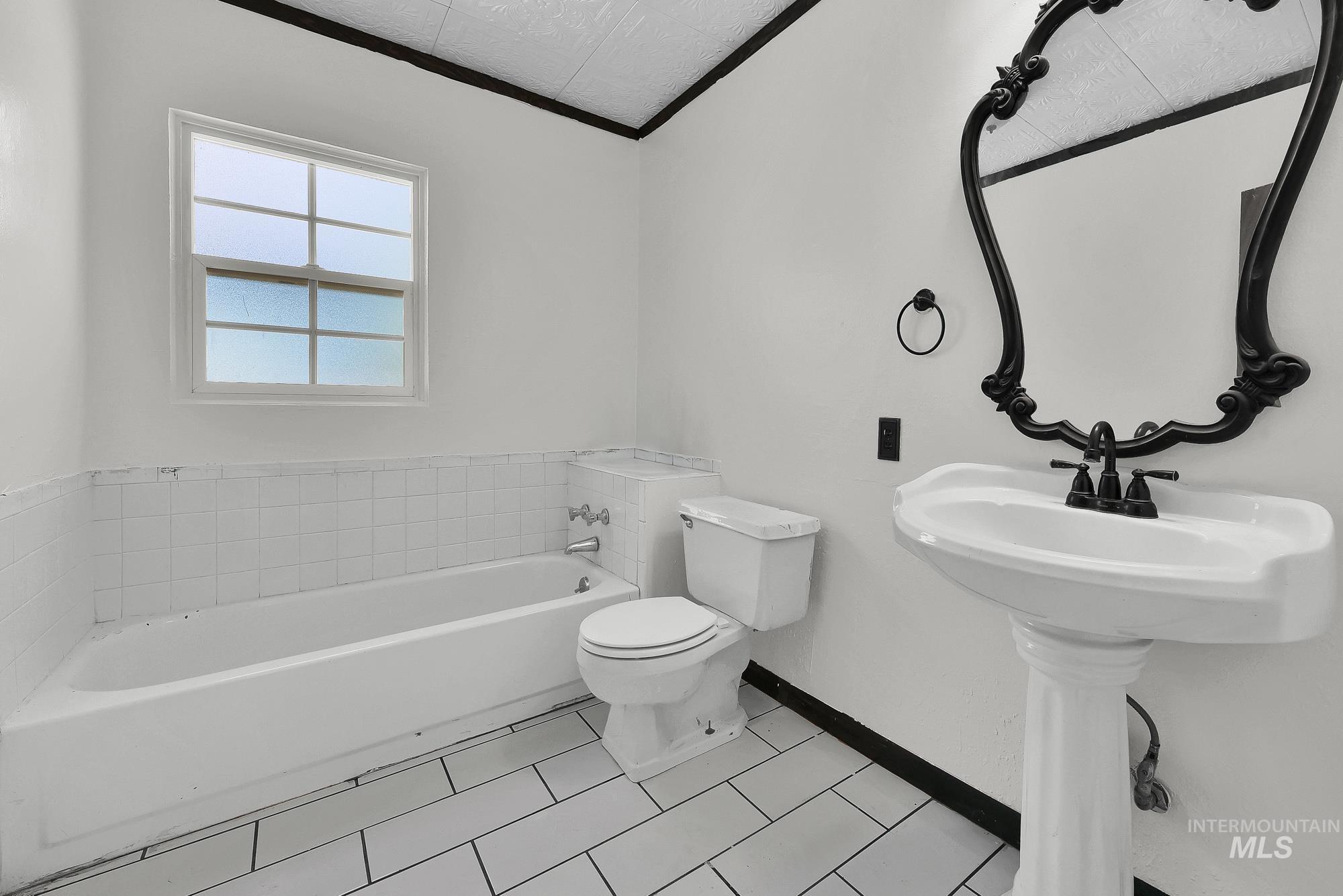 808 North A Street Parma, ID 83660 - Photo 14 of 29 Full bathroom featuring a pedestal sink with a matte black faucet, an ornate black-framed mirror, a toilet, and a white bathtub with tile surround