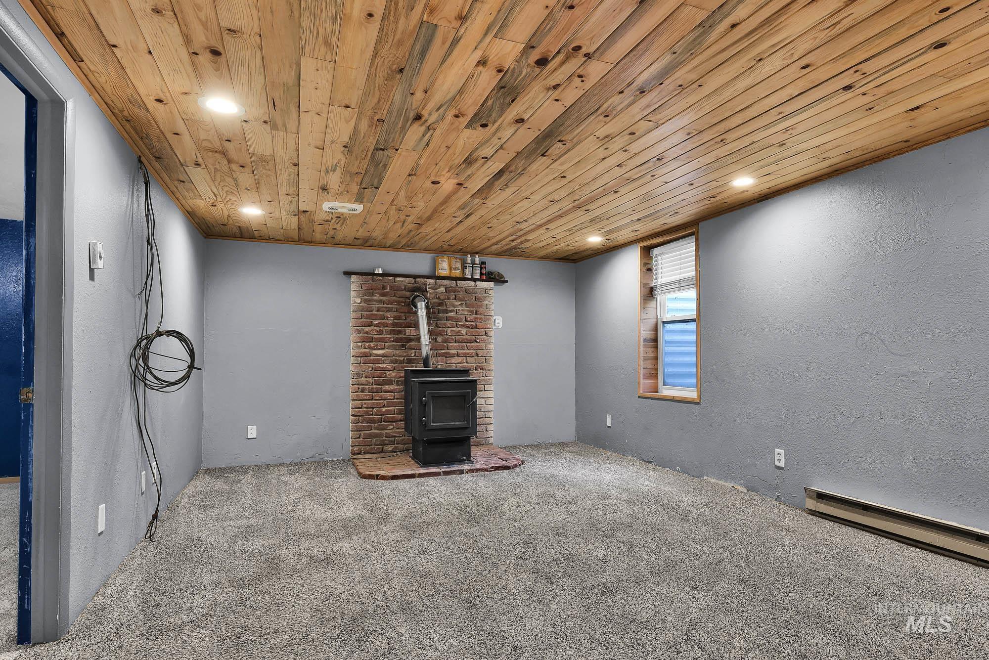 808 North A Street Parma, ID 83660 - Photo 16 of 29 Room featuring a wood-panel ceiling with recessed lighting, a brick fireplace with a wood-burning stove, and gray textured walls