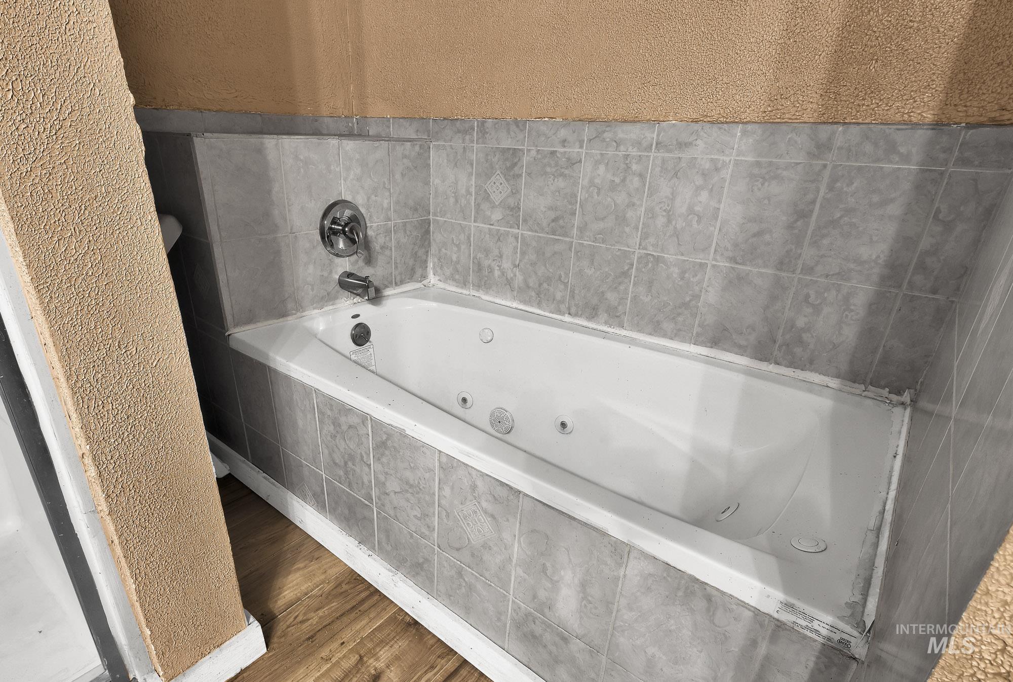 808 North A Street Parma, ID 83660 - Photo 23 of 29 Built-in jetted tub with chrome fixtures, surrounded by gray tile and a textured wall finish