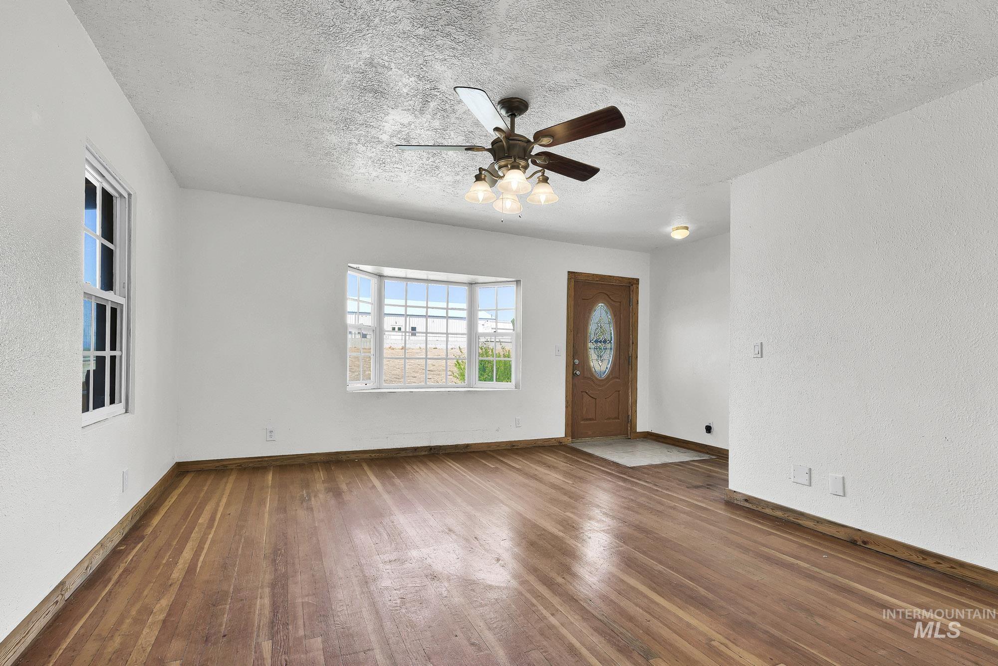 808 North A Street Parma, ID 83660 - Photo 4 of 29 Spacious living area featuring wood-finish flooring, a bay window, and a prominent ceiling fan with integrated lighting