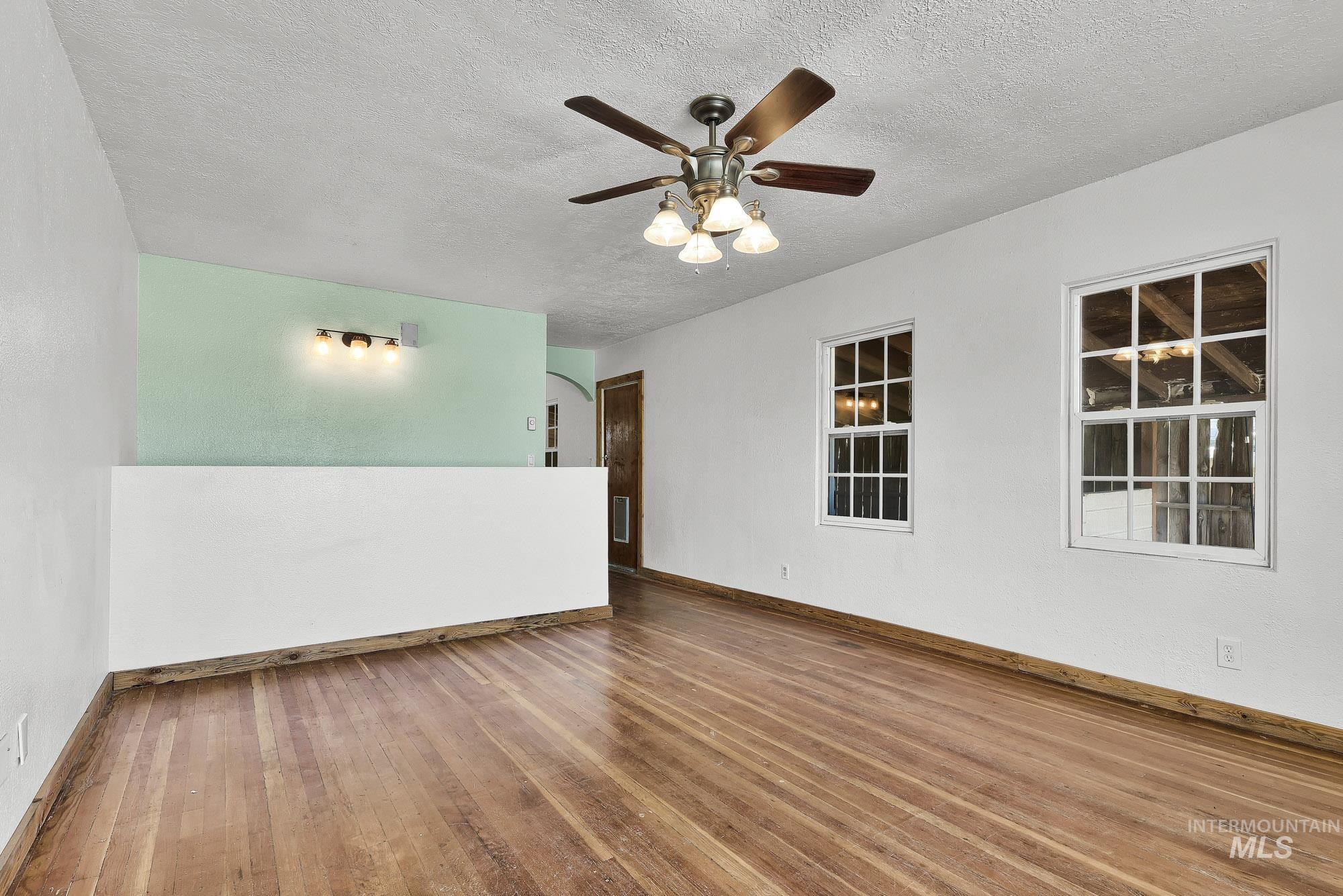 808 North A Street Parma, ID 83660 - Photo 5 of 29 Spacious room featuring wood-finish flooring, two large windows with mullions, and a ceiling fan with integrated lighting