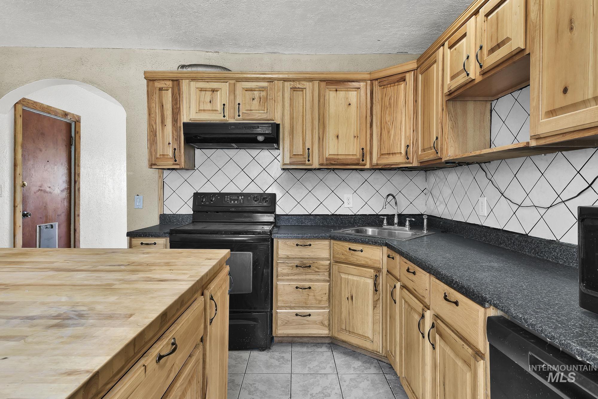 808 North A Street Parma, ID 83660 - Photo 9 of 29 Kitchen featuring wood cabinetry, dark countertops, tiled backsplash with diamond pattern, and a central wood-finish island